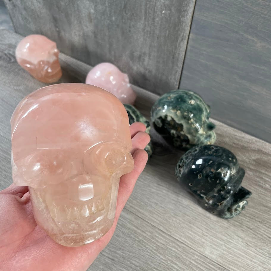 Close up of rose quartz skull with rose quartz and Kabamba jasper skulls in the background.