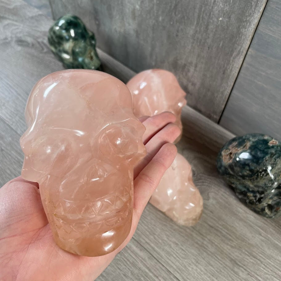 Close up of rose quartz skull with rose quartz and Kambaba jasper skulls in the background.
