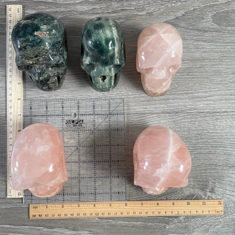 Lot of 5 crystal skulls; three rose quartz and two Kabamba jasper. With grid and rulers for size reference.