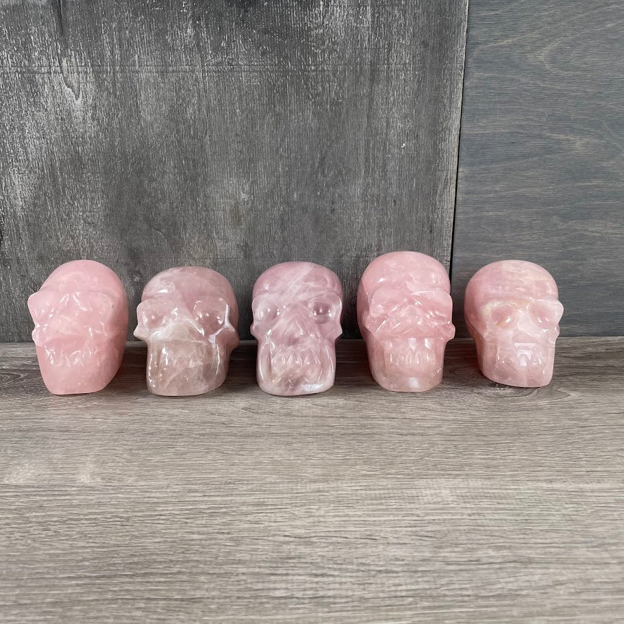 Lot of five rose quartz skulls facing forward.