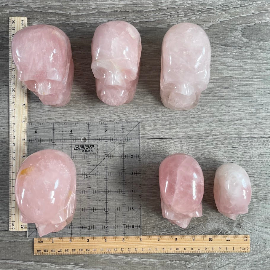 Lot of 6 rose quartz skulls, with grid and rulers for size reference.