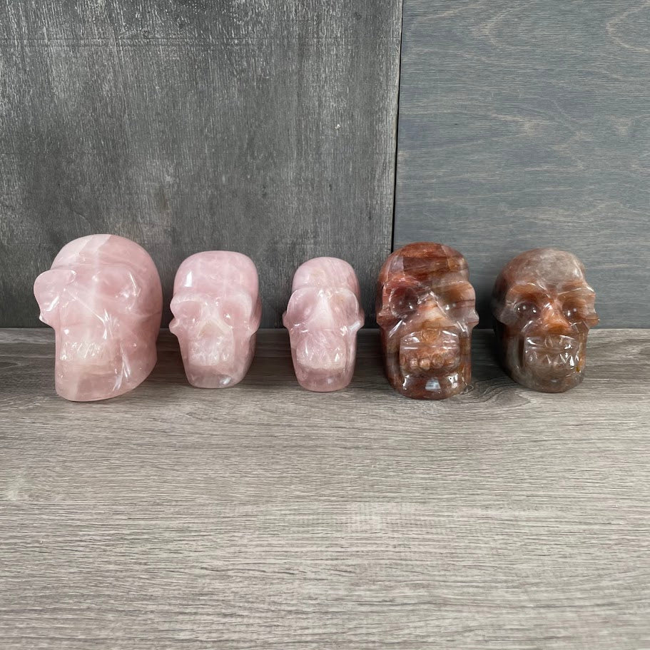 Lot of three rose quartz skulls and two hematoid quartz skulls; facing forwards.