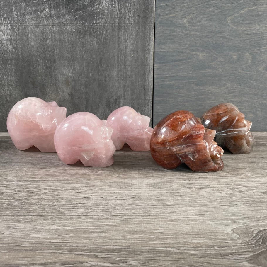 Lot of three rose quartz skulls and two hematoid quartz skulls; facing sideways.