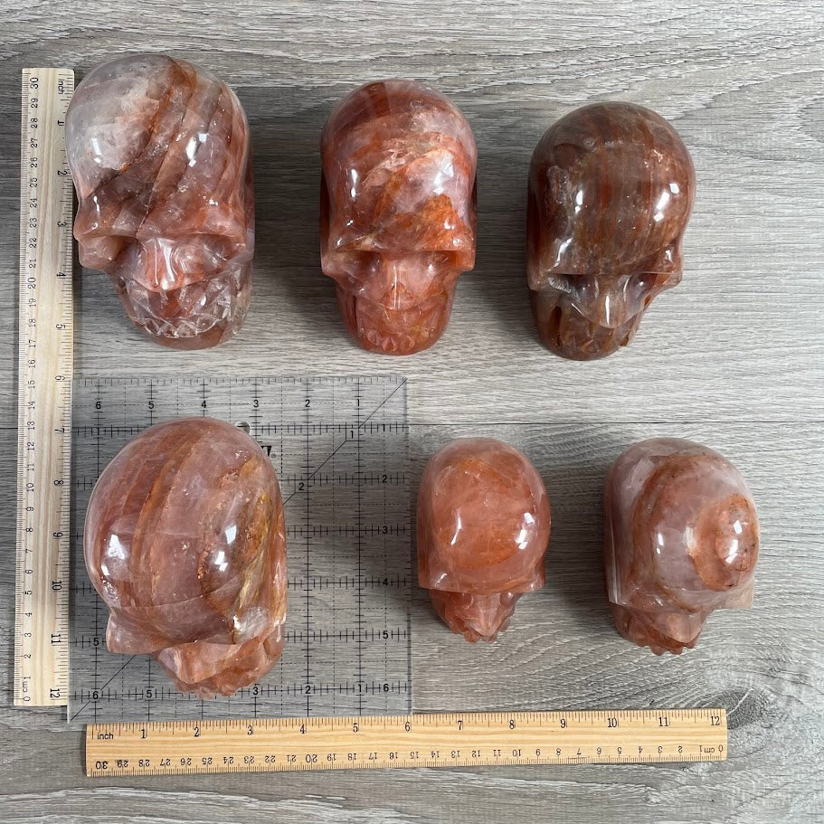 Lot of six hematoid quartz skulls, with grid and rulers for size reference.