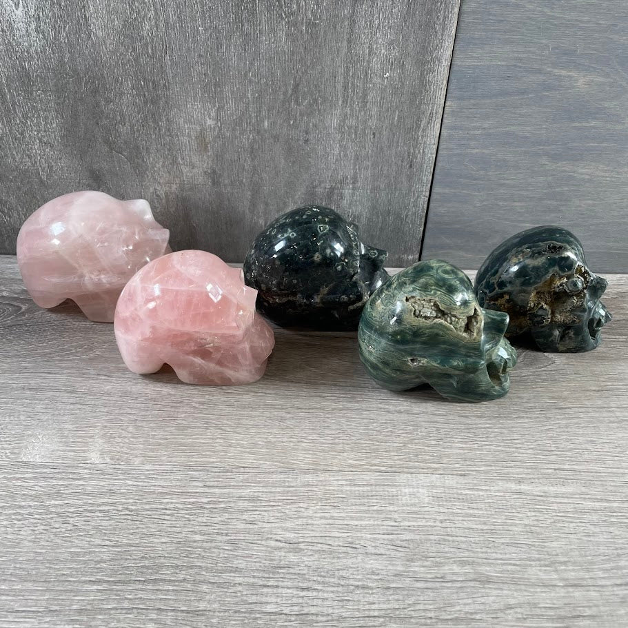 Lot of three Kambaba jasper skulls and two rose quartz skulls; facing sideways.