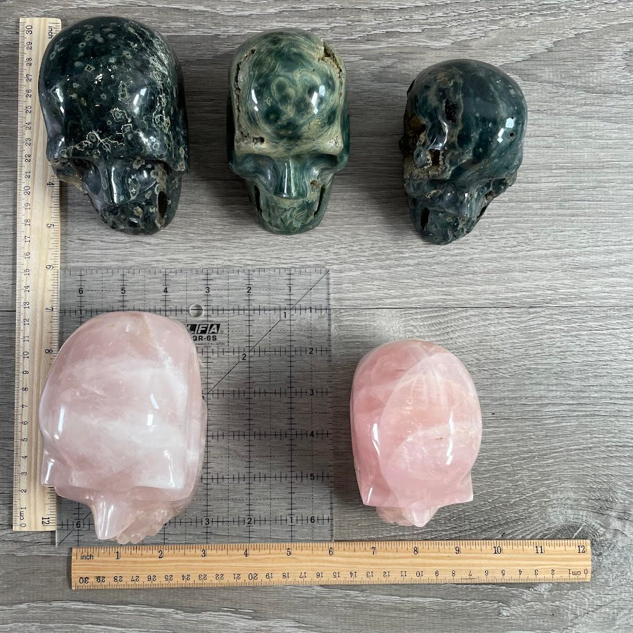 Lot of five crystal skulls: three Kambaba jasper and two rose quartz. With grid and rulers for size reference.