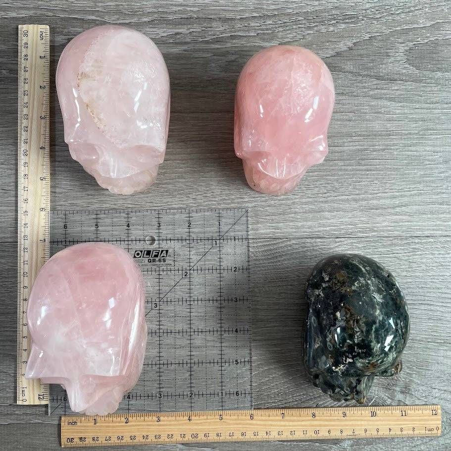 Lot of four crystal skulls: three rose quartz and one Kambaba jasper. With grid and rulers for size reference.