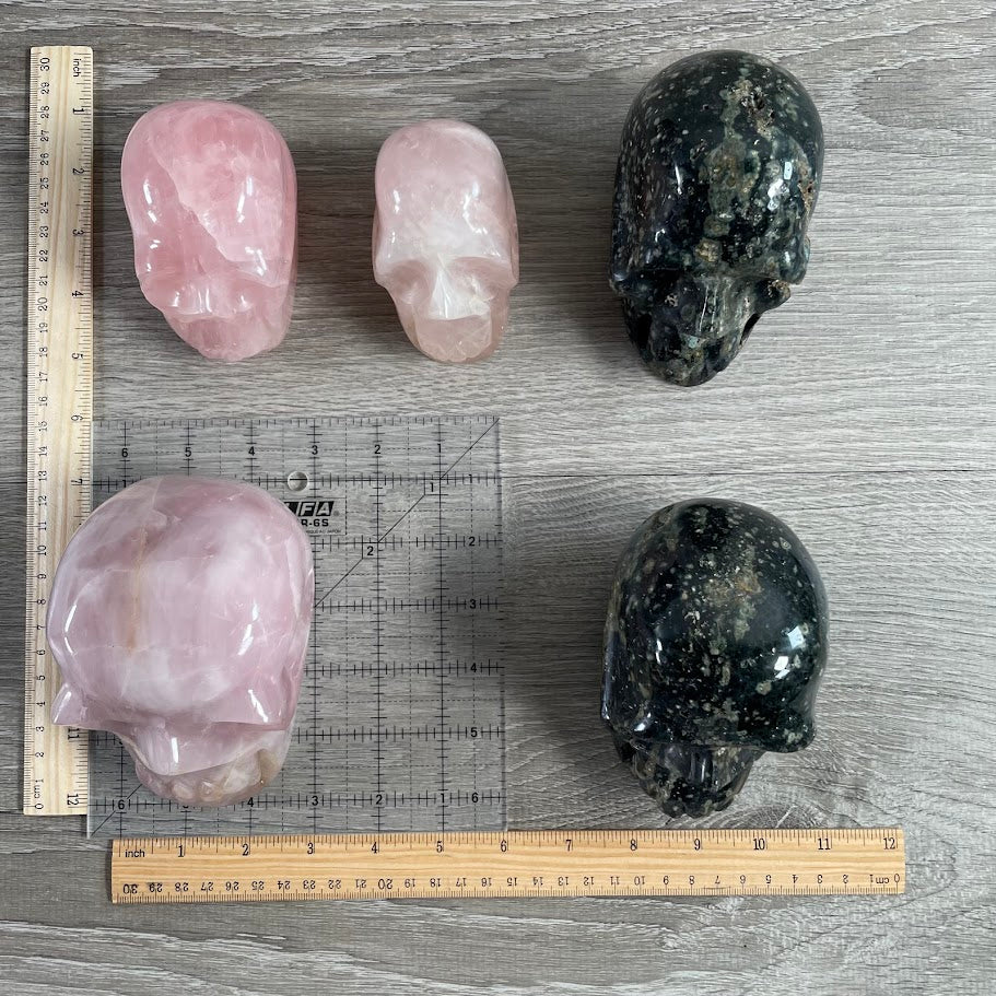 Lot of five crystal skulls: three rose quartz and two Kabamba jasper. With grid and rulers for size reference.