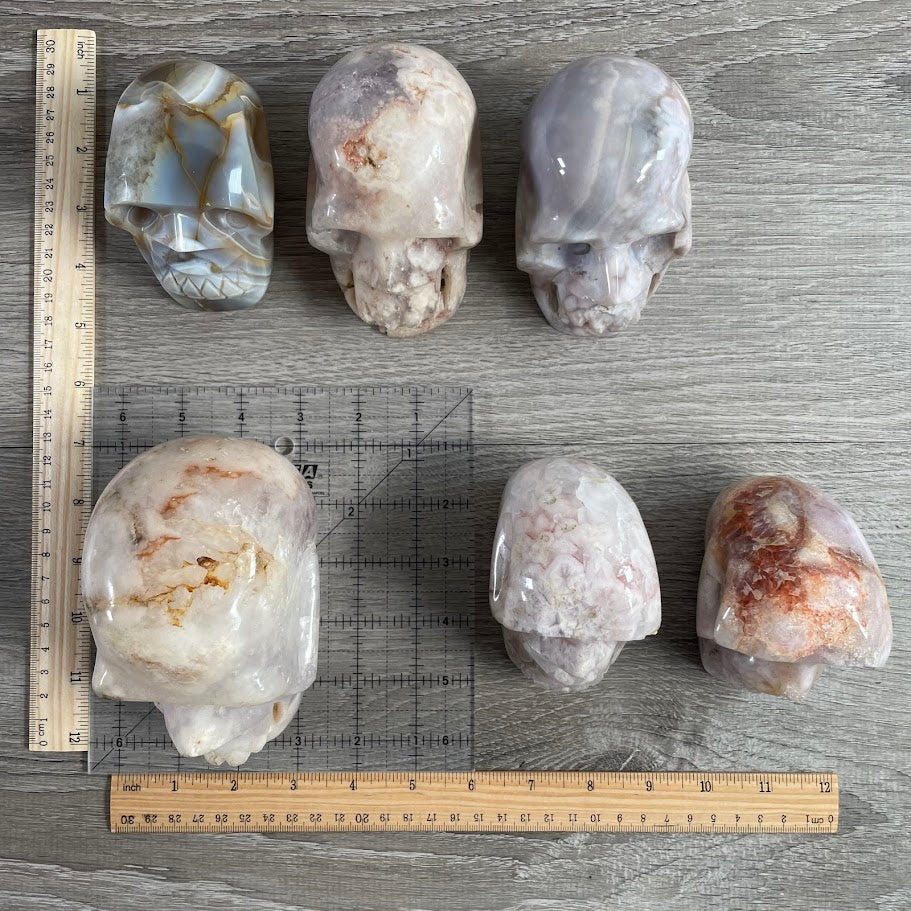 Lot of six crystal skulls: four quartz and two agate. With grid and rulers for size reference.