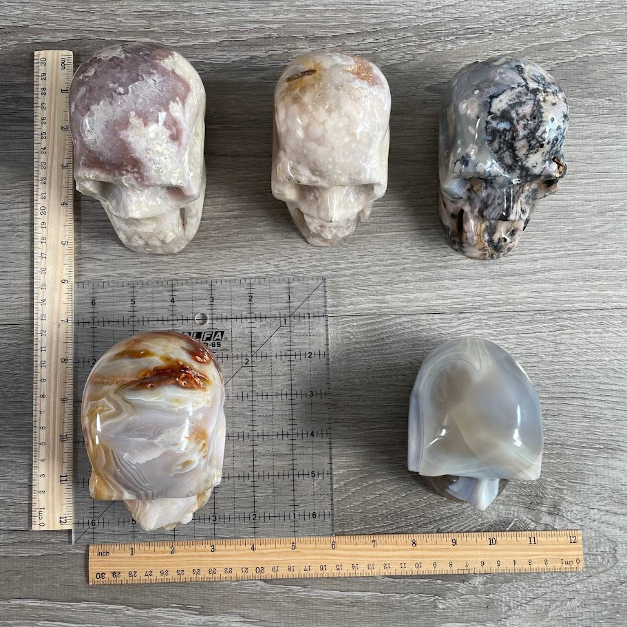 Lot of five crystal skulls: three quartz and two agate. With grid and rulers for size reference.
