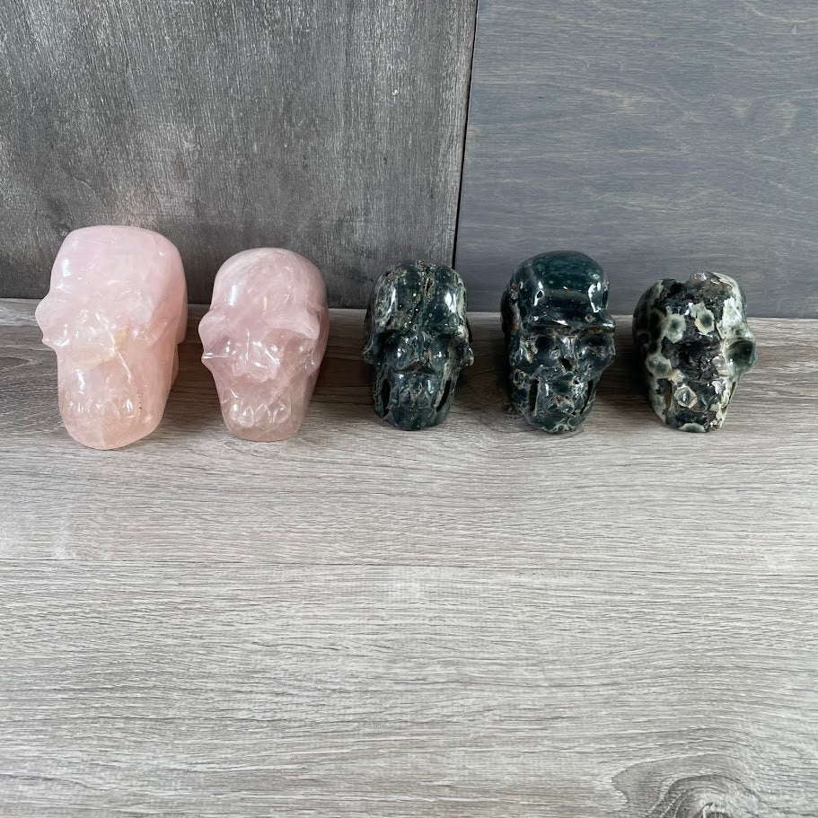 Lot of three Kambaba jasper skulls and two rose quartz skulls; facing forwards.