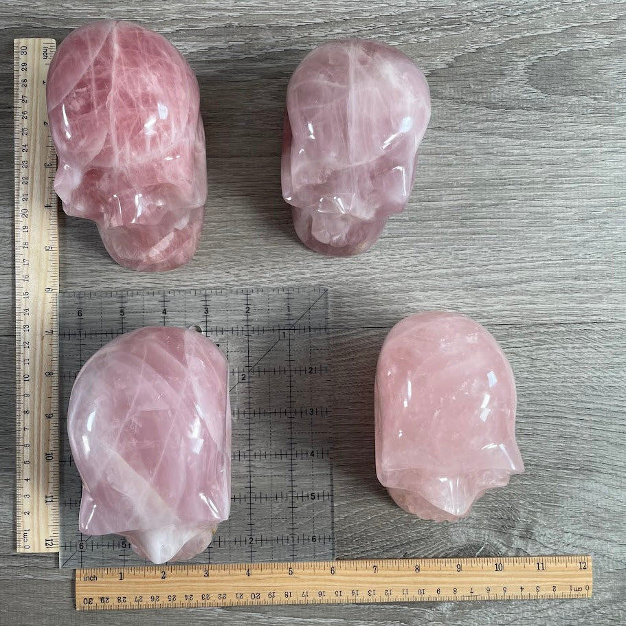 Lot of four rose quartz skulls with grid and rulers for size reference.