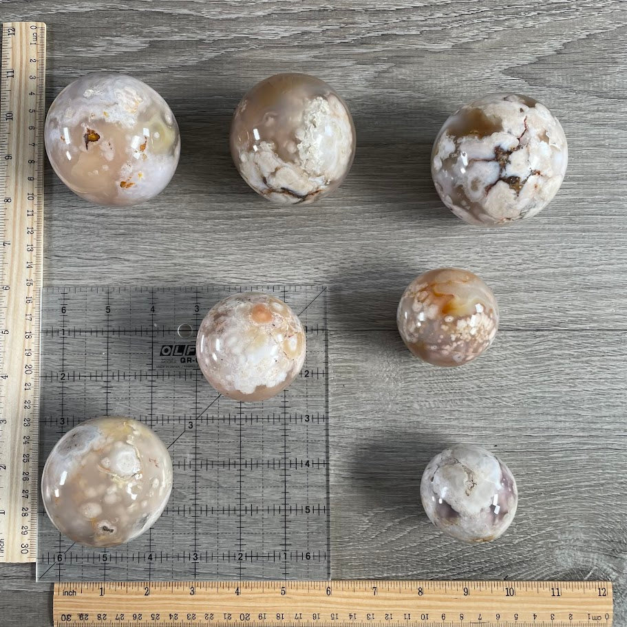 Lot of seven flower agate spheres with grid and rulers for size reference.
