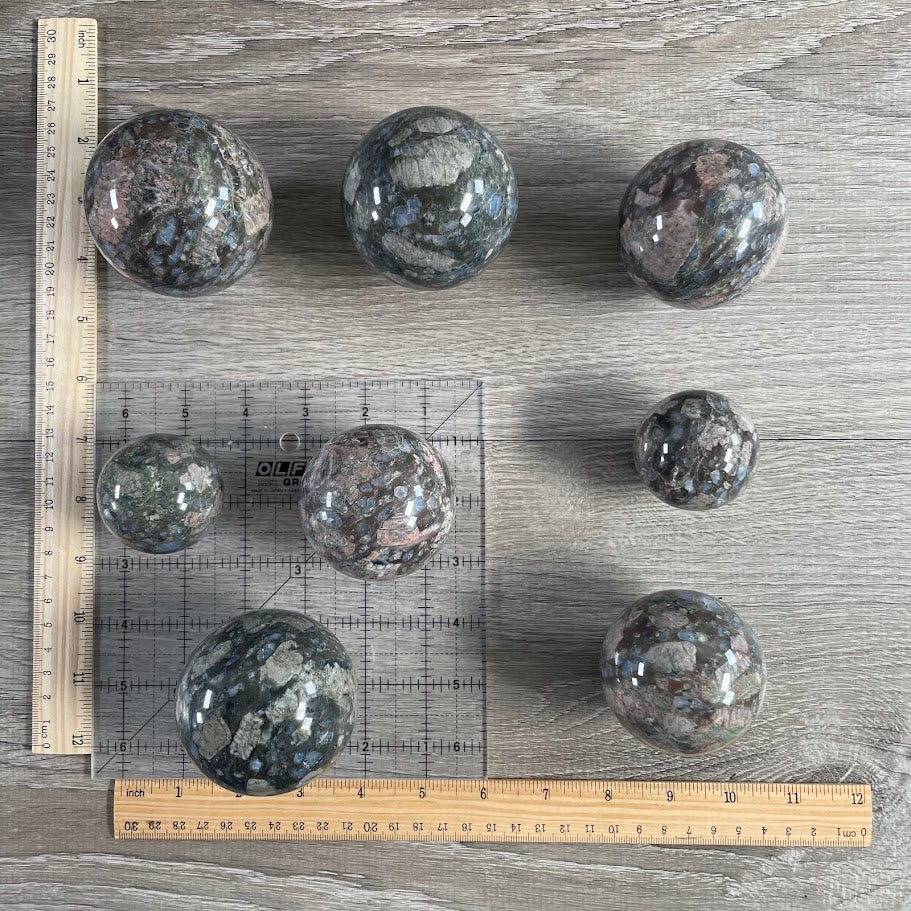 Lot of eight que sera spheres with grid and rulers for size reference.