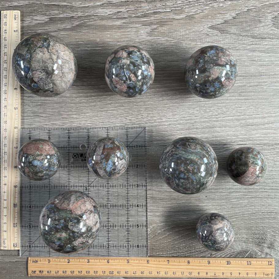Lot of nine que sera spheres with grid and rulers for size reference.