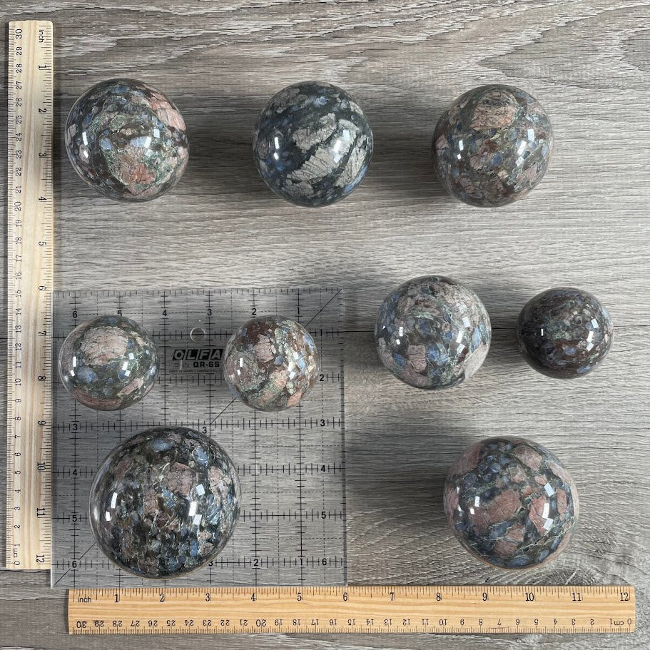 Lot of nine que sera spheres with grid and rulers for size reference.