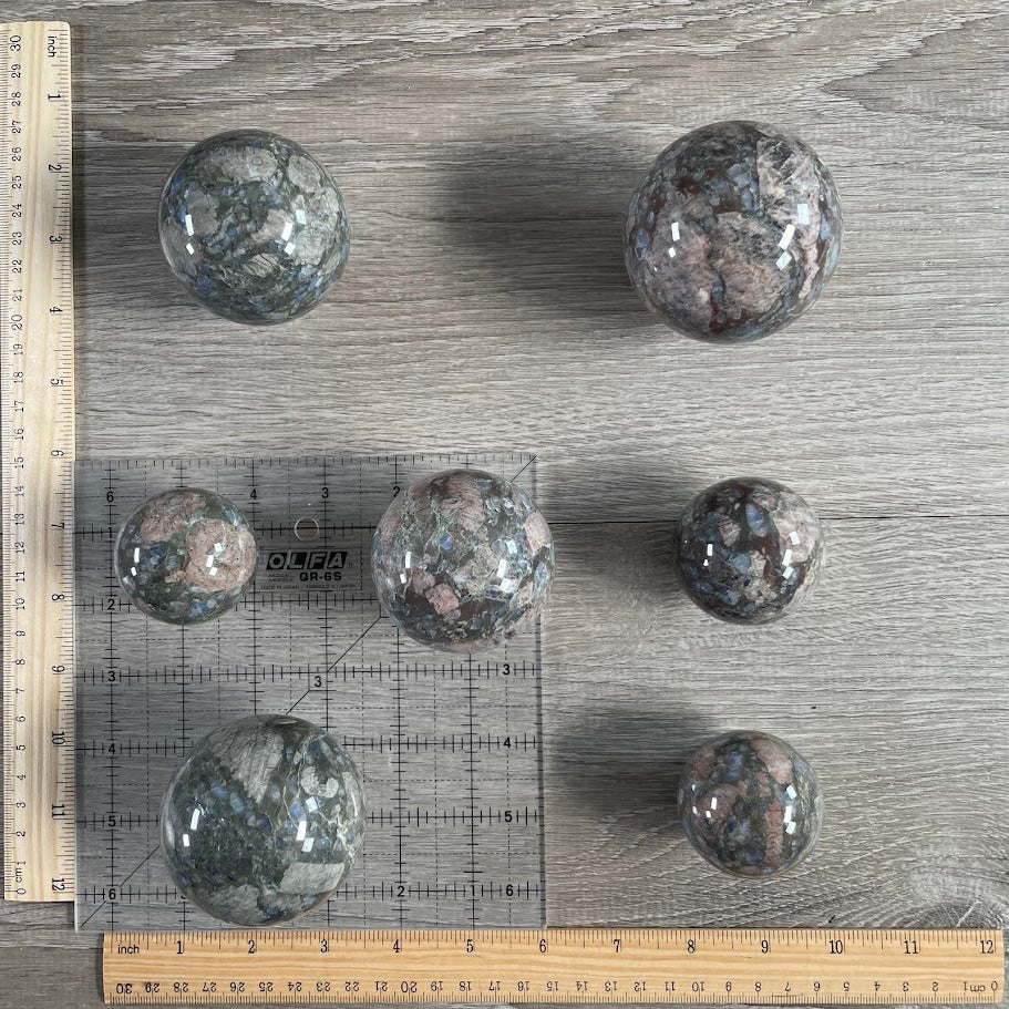 Lot of seven que sera spheres with grid and rulers for size reference.
