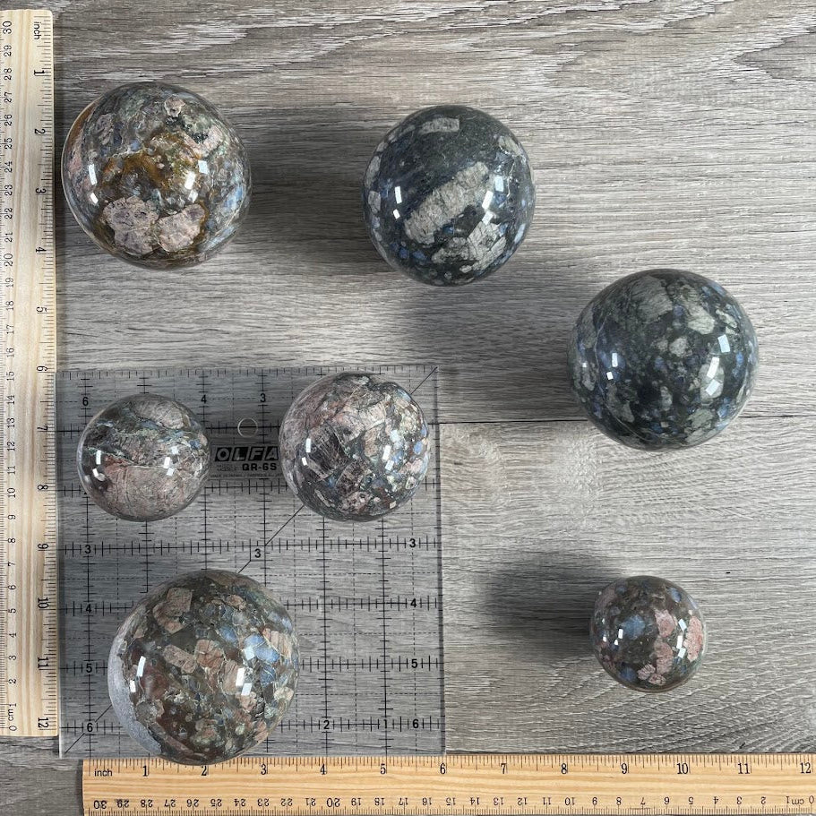 Lot of seven que sera spheres with grid and rulers for size reference.