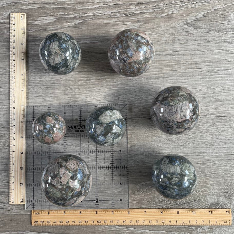 Lot of seven que sera spheres with grid and rulers for size reference.