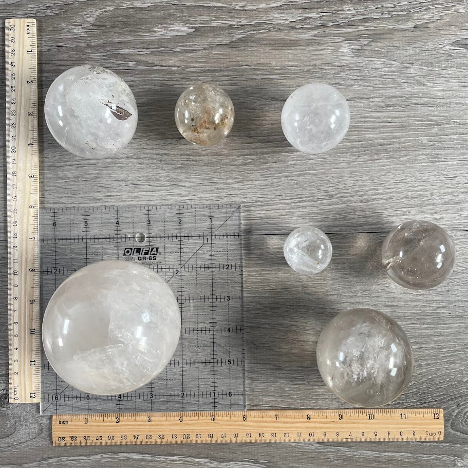 Lot of seven quartz spheres with grid and rulers for size reference.