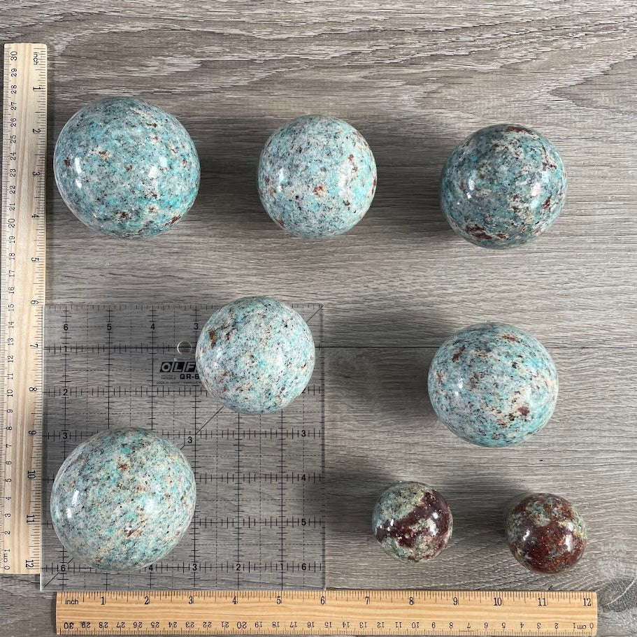 Lot of eight amazonite with biotite spheres with grid and rulers for size reference.