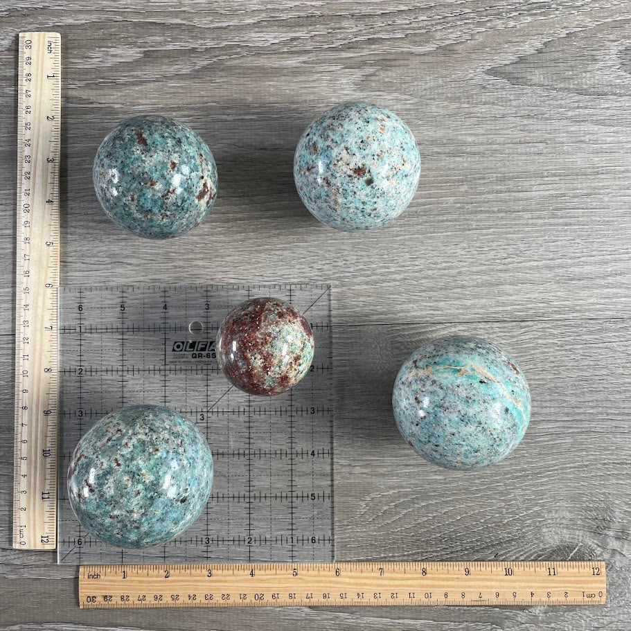 Lot of five amazonite with biotite spheres with grid and rulers for size reference.