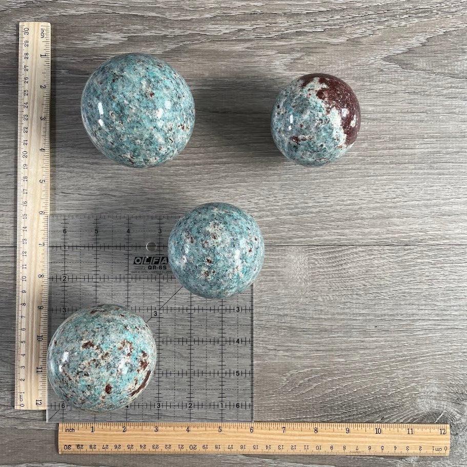 Lot of four amazonite with biotite spheres with grid and rulers for size reference.