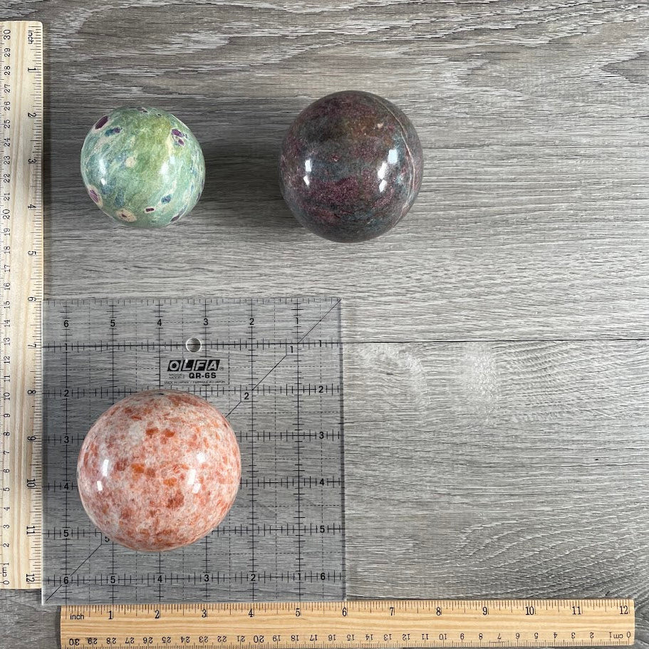 Lot of three: one ruby in zoisite sphere, one ruby in kyanite sphere and one sunstone sphere with grid and rulers for size reference.