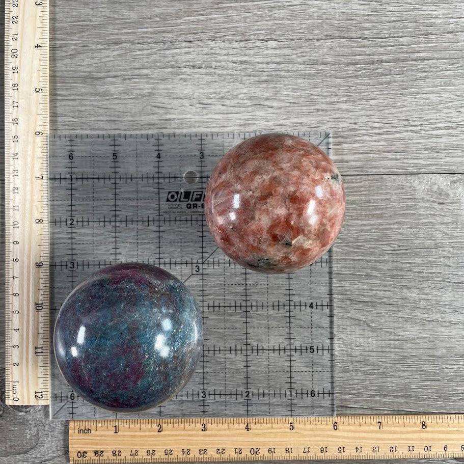 Lot of two: one ruby in kyanite sphere, one sunstone sphere. With grid and rulers for size reference.