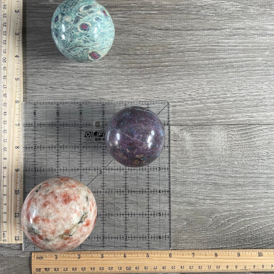 Lot of three: one ruby in zoisite sphere, one ruby in kyanite sphere and one sunstone sphere. With grid and rulers for size reference.
