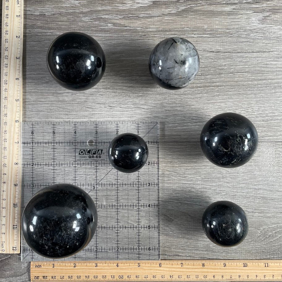 Lot of six black tourmaline spheres with grid and rulers for size reference.