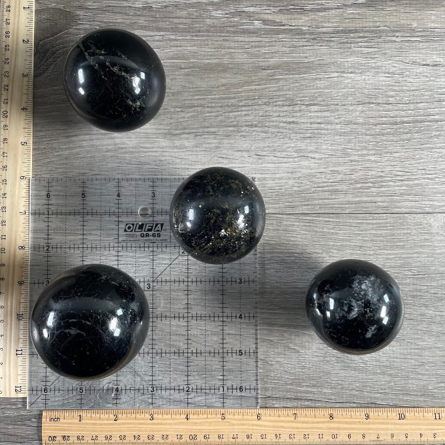 Lot of four black tourmaline spheres with grid and rulers for size reference.