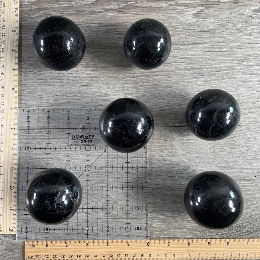 Lot of six black tourmaline spheres with grid and rulers for size reference.