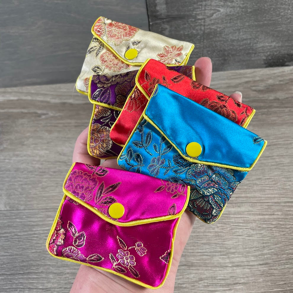 Assorted colorful satin brocade crystal storage pouches with snap closure for gemstones, crystals, jewelry, and small gifts.