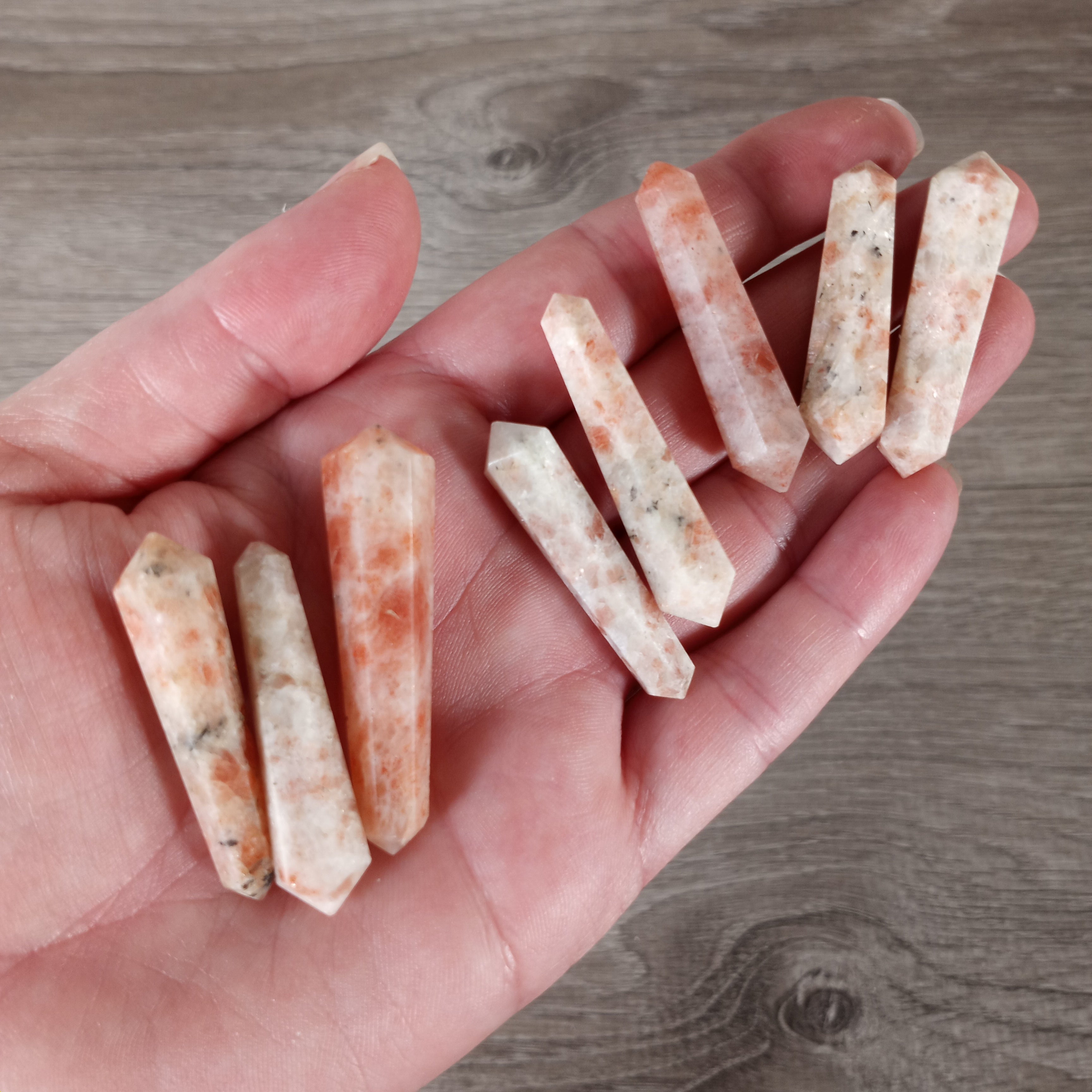 Small double terminated sunstone wand on a hand with grey background - premium wholesale crystal supply