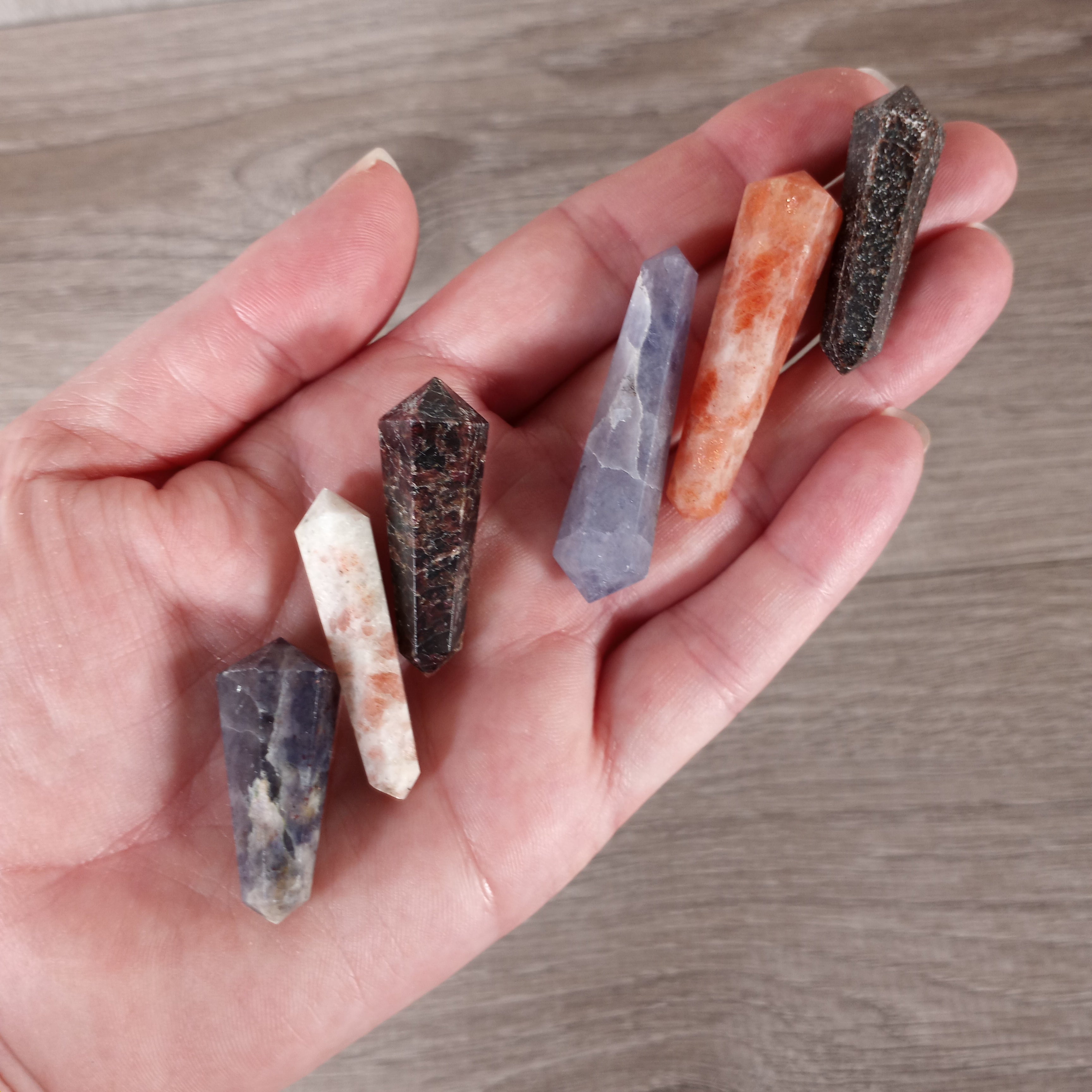 Small double terminated garnet iolite and sunstone wands on a hand with a grey background - perfect for wholesale buyers