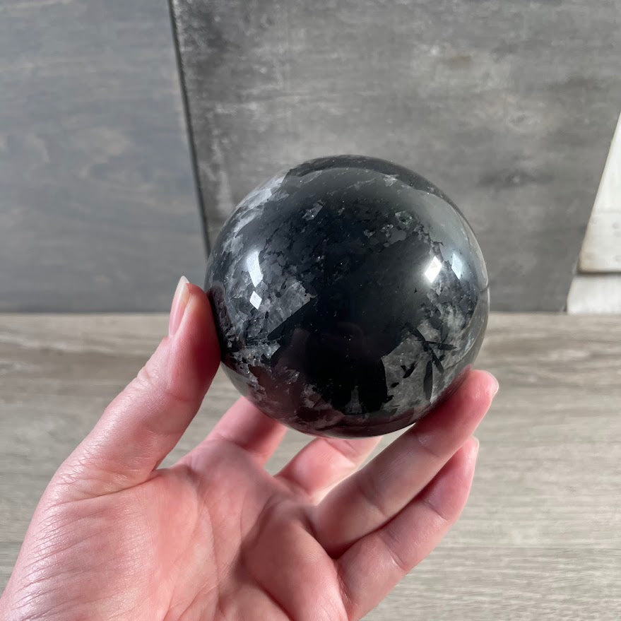 Polished gemstone sphere made from quartz with black tourmaline inclusions