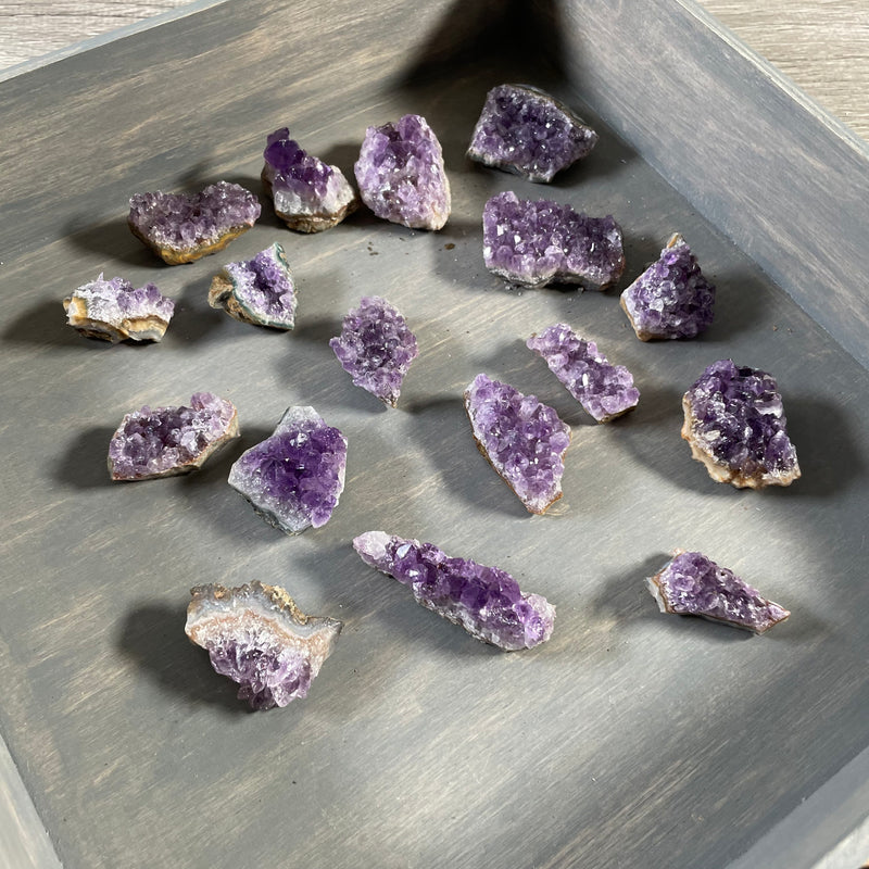 Display of multiple Brazilian amethyst clusters from a 1-pound bulk lot on a grey wooden box.