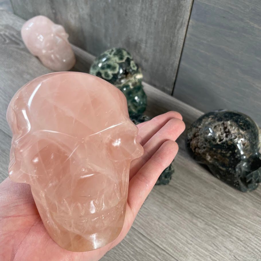 Close up of rose quartz skull with rose quartz and Kambaba jasper skulls in the background. 