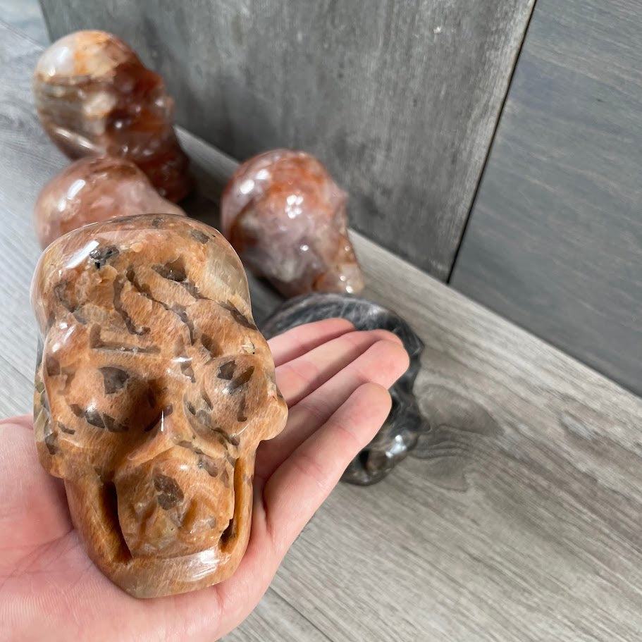 Close up of peach moonstone skull with other skulls in the background. 