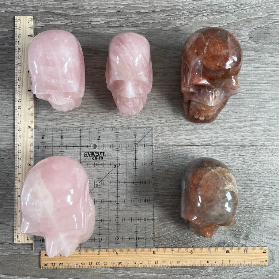 Lot of five crystal skulls: three rose quartz, and two hematoid quartz. With grid and rulers for size reference.