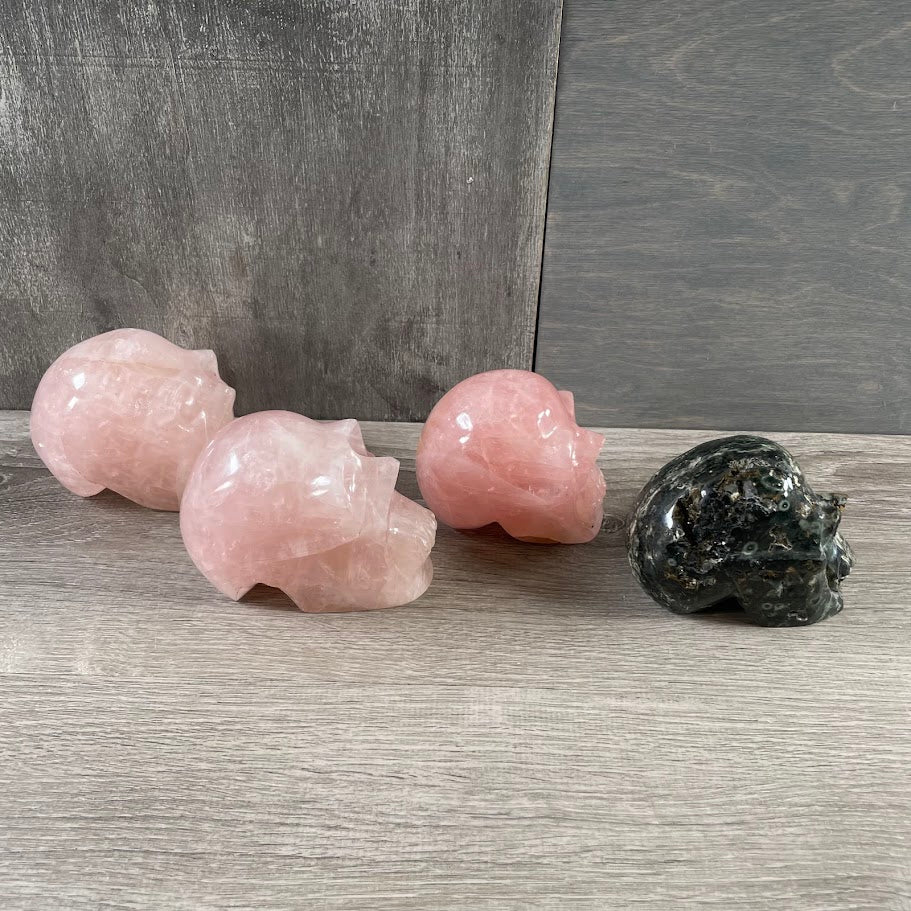 Lot of three rose quartz skulls and one Kambaba jasper skull; facing sideways.