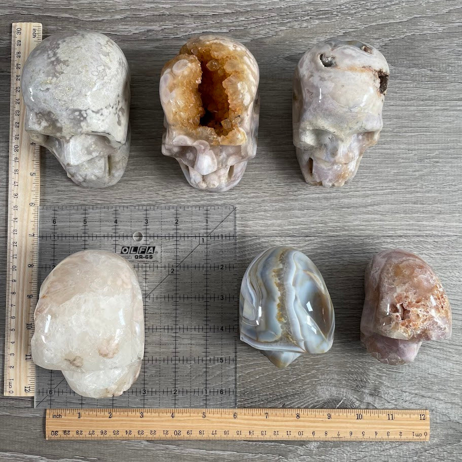 Lot of five quartz and one agate skull, with grid and rulers for size reference. 