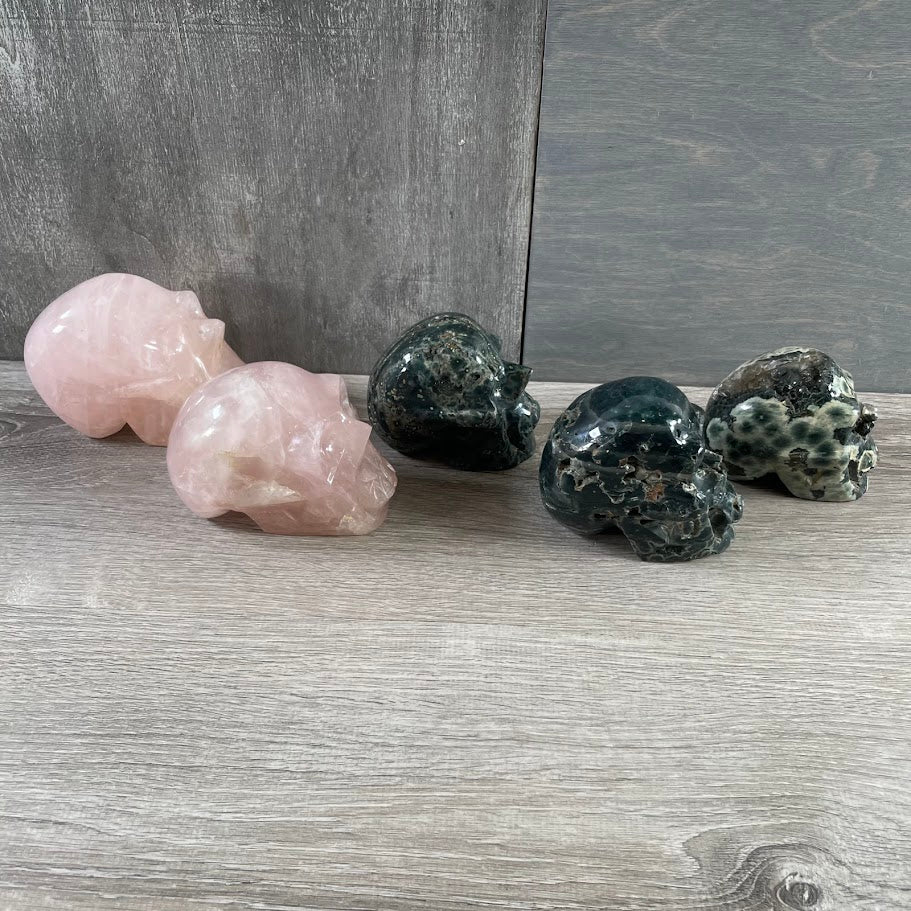 Lot of three Kambaba jasper skulls and two rose quartz skulls; facing sideways. 