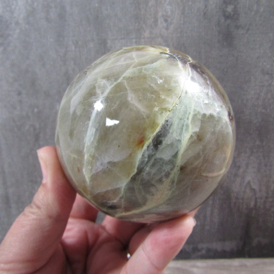 Large moonstone garnierite sphere with green hues and polished surface on display