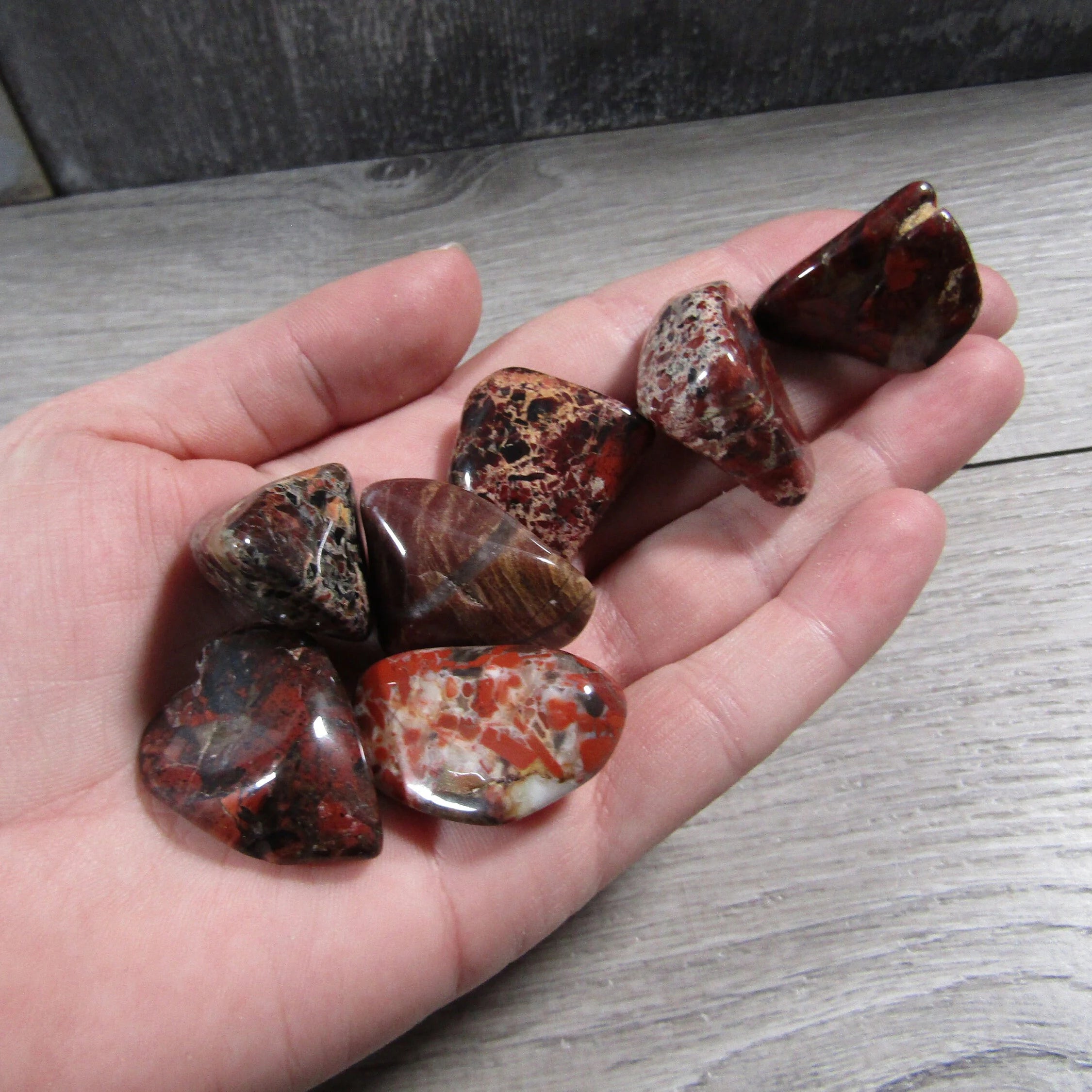 Hand holding polished brecciated red jasper tumbled stones for size reference.