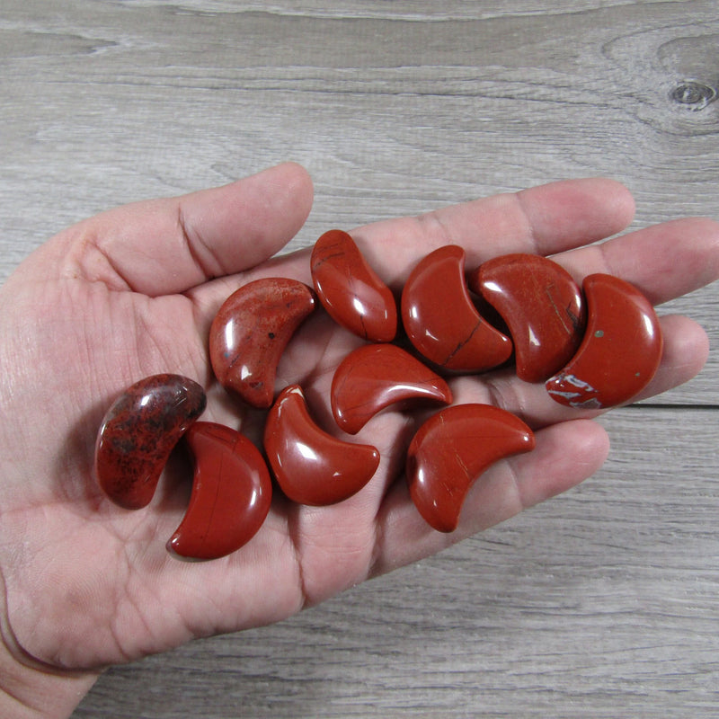 Red jasper crescent moon wholesale on a hand with a grey background - Keystone Crystals