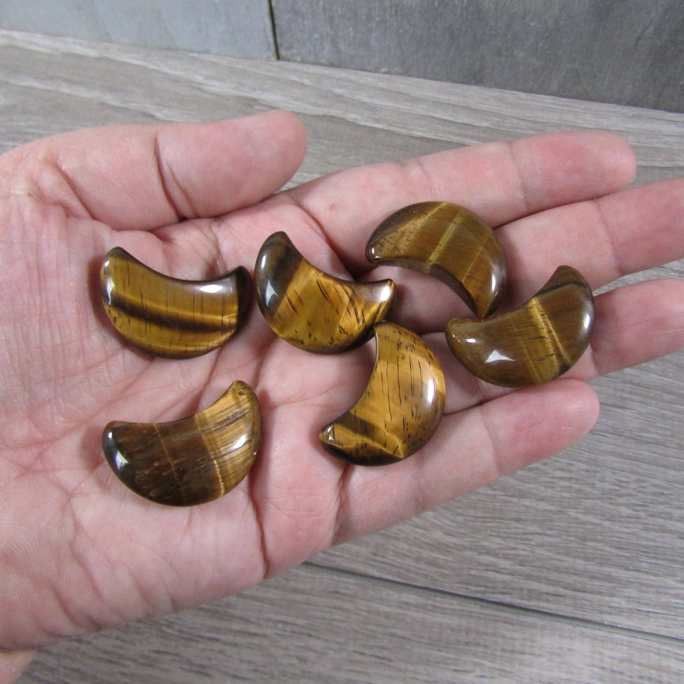 Tiger eye crescent moon wholesale displayed on a hand with a grey background - Keystone Crystals