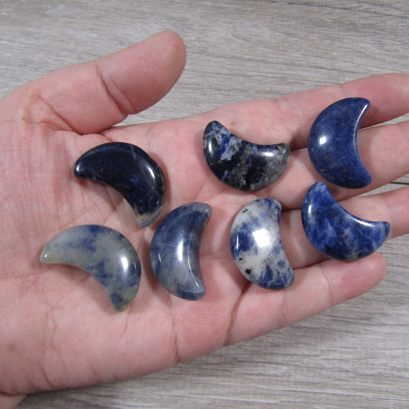 Sodalite crescent moon displayed on a hand with a grey background - Keystone Crystals