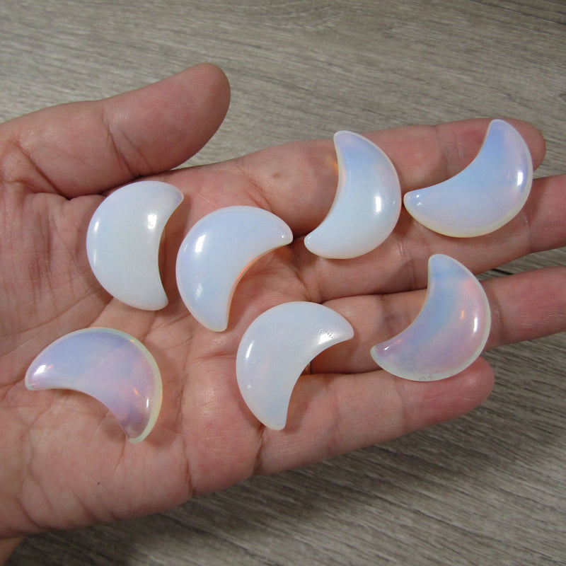 Opalite crescent moon displayed on a hand with a grey background - Keystone Crystals